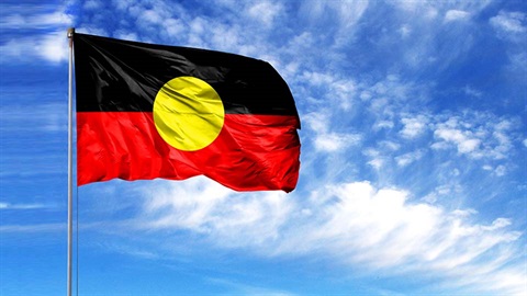 Aboriginal flag against blue sky with white clouds