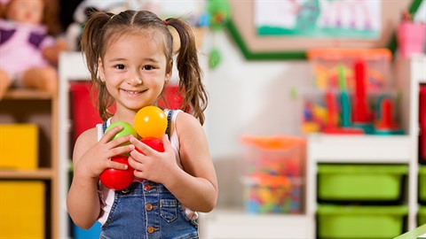 Young girl holding plastic balls at kindergarten