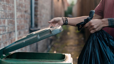 Image of person putting rubbish bag in bin