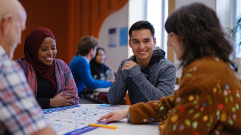 Two women and two men sit around a circular table. They are smiling and one woman is pointing at a large poster in the centre of the table.