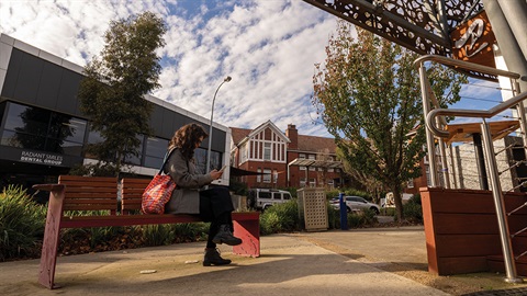 A young person sits on a bench outside of a building.jpg