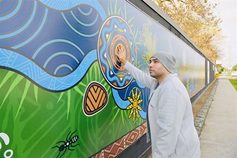 Dixon Patten standing with his mural on the construction site fencing