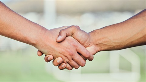 Two hands shaking with a football pitch in background