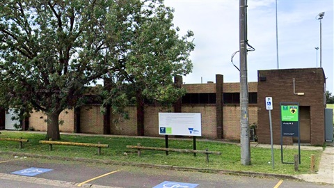 Brown brick building with grass and tree in front. A green sign says JC Donath Reserve