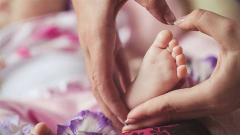 mother's hands making heart shape around baby's foot