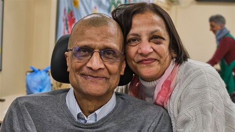 Two older residents: the male sits in a wheelchair and the woman stands by his side.