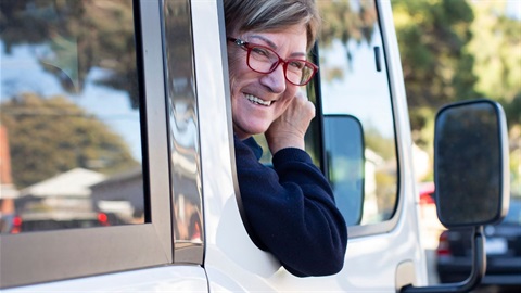 A woman leans out of the window of a mini bus and smiles.