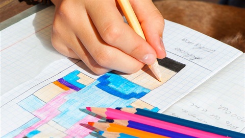 Child drawing coloured blocks on grid paper