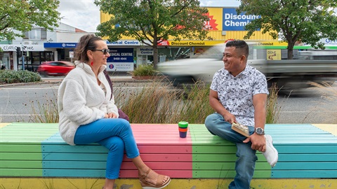 Two people sitting on a bench having a coffee catchup