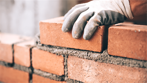 Hands laying bricks to build structure