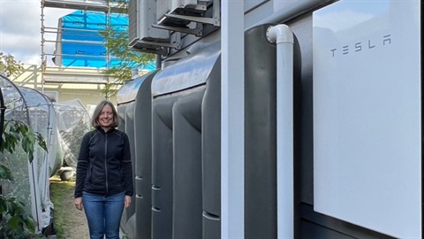Helen standing next to water tanks and a solar powered battery