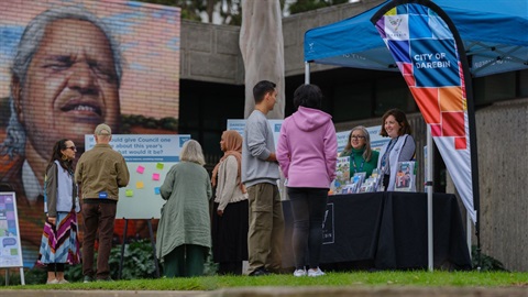 People standing in front of a marquee with Darebin branding and talking to people behind a table