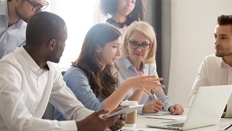 Six people gathered around a table, listening to the person in the centre