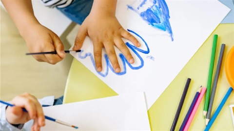 Young child painting an outline of their hand in blue on white paper