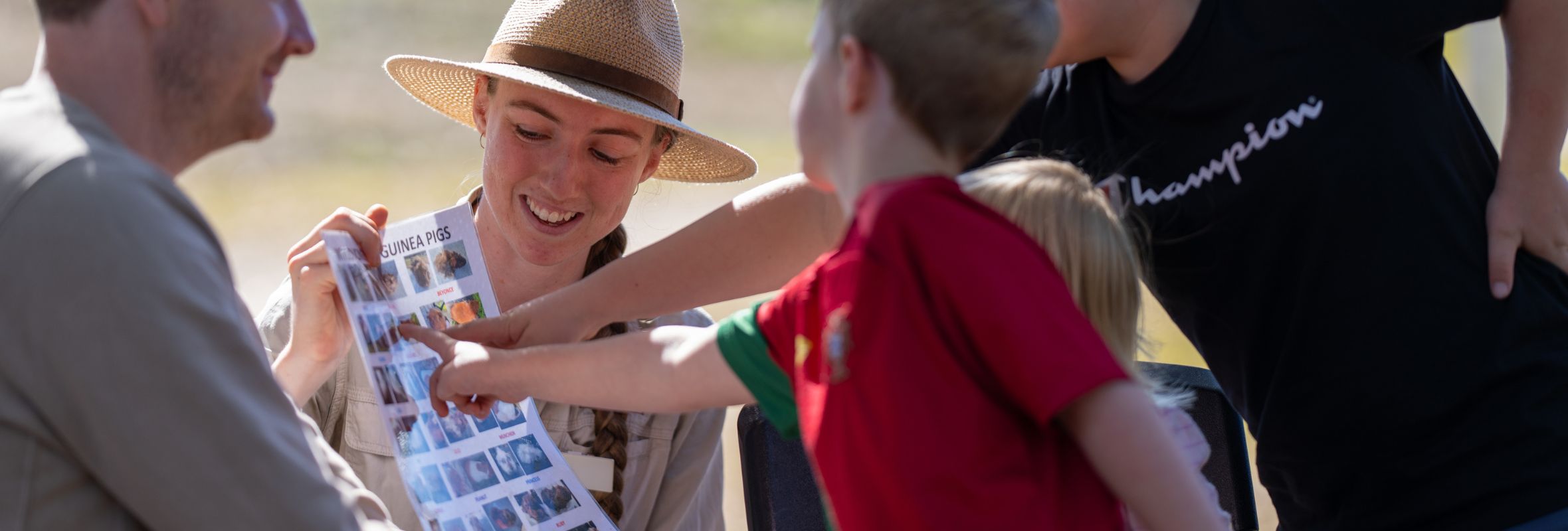 A group of 3 children pointing to a poster with guinea pig photos at Bundoora Park Farm