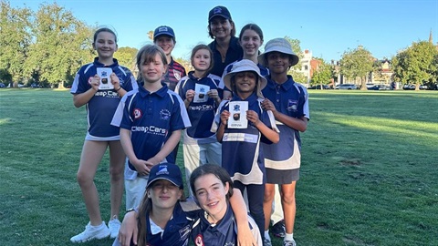A group of young firls wearing blue team shirts standing and smiling with their coach