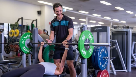A male staff member from Reservoir Leisure Centre assists a woman with lifting weights