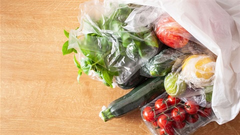 Fruit and vegetables wrapped in plastic and placed in a white plastic shopping bag
