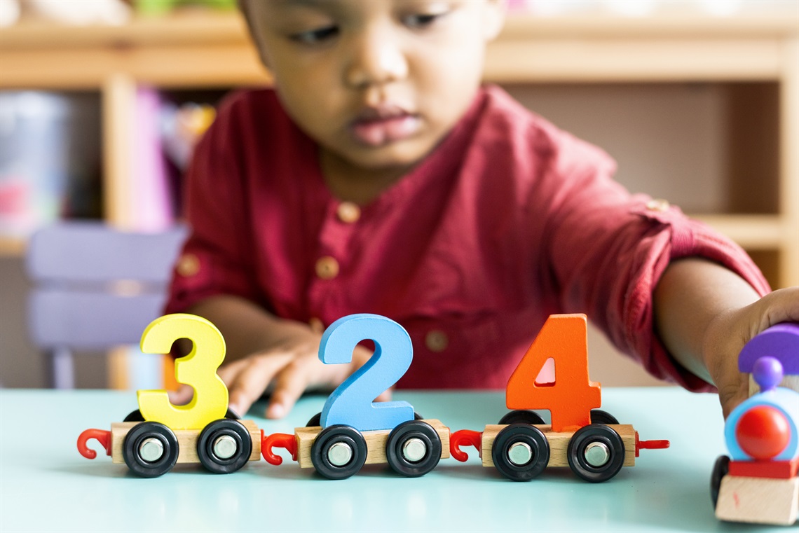 A little boy in the background playing with a toy with number blocks in the foreground