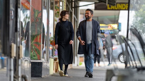 Couple walking along local street with shop windows in background